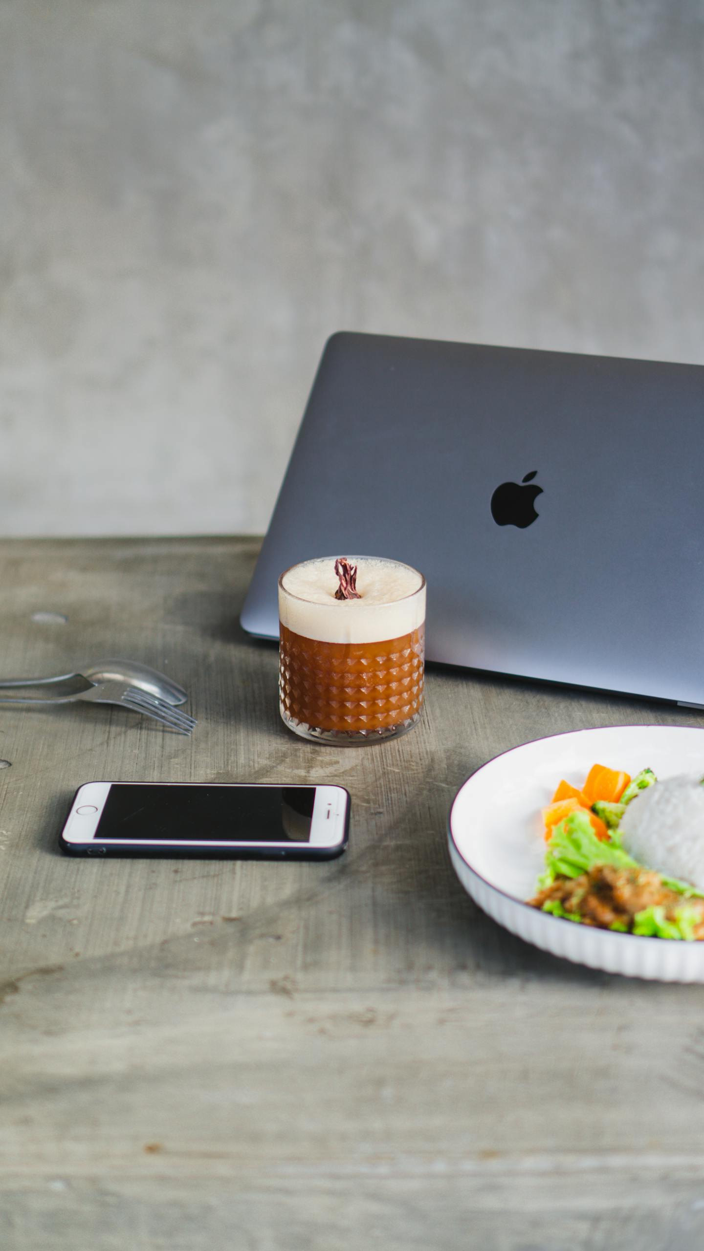 A contemporary workspace featuring a laptop, iced coffee, and a healthy lunch plate.