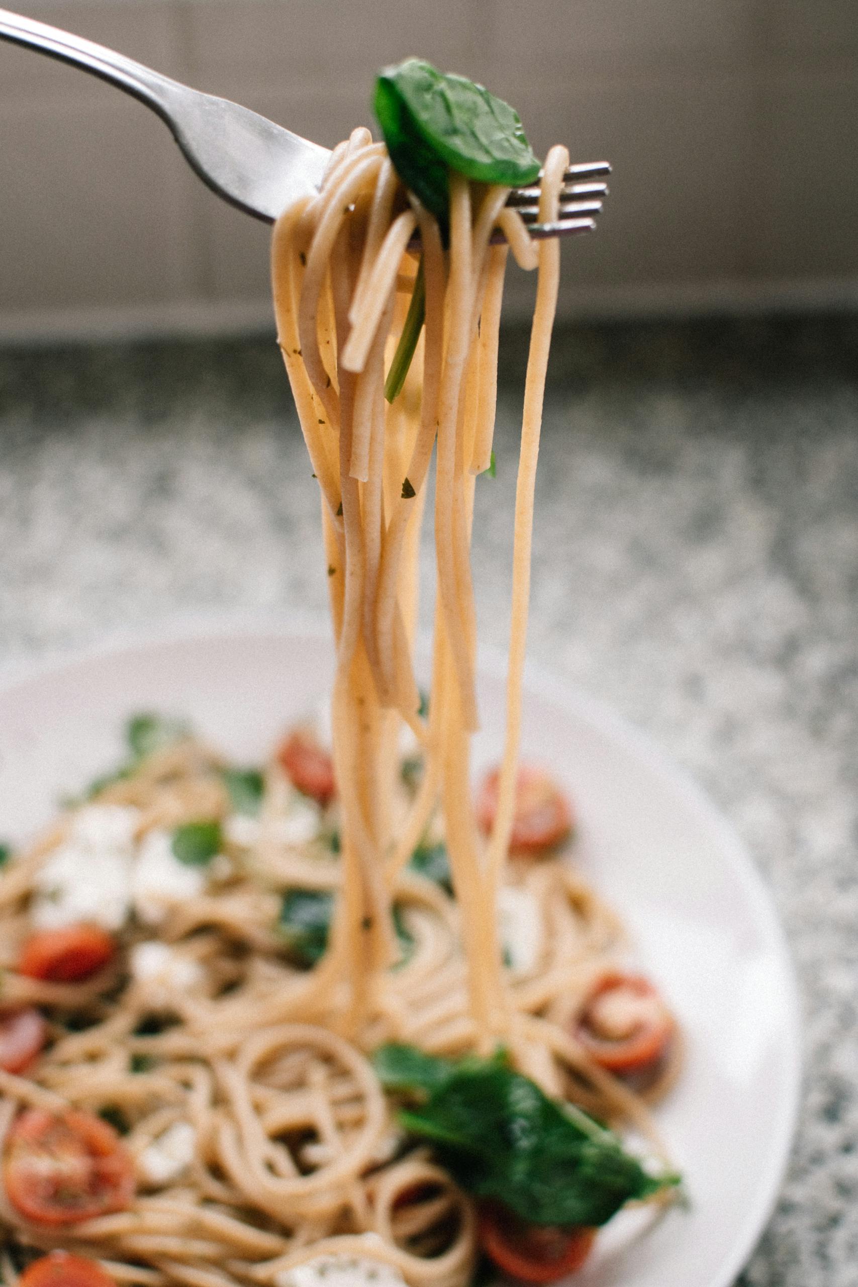 Close-up of freshly cooked spaghetti with cherry tomatoes, spinach, and mozzarella cheese on a plate.
