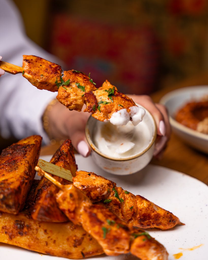 Close-up of grilled chicken skewers being dipped in sauce, perfect for lunch.