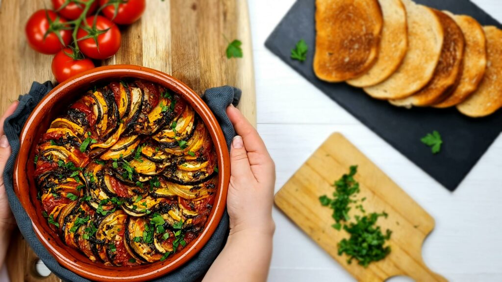 Colorful homemade ratatouille in a ceramic bowl with tomatoes and toast, perfect for a rustic meal.