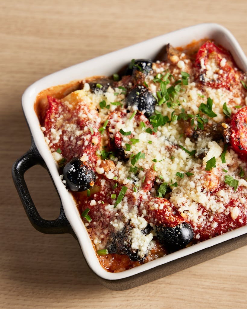 Delicious Italian baked pasta topped with cheese, tomatoes, and olives in a casserole dish.