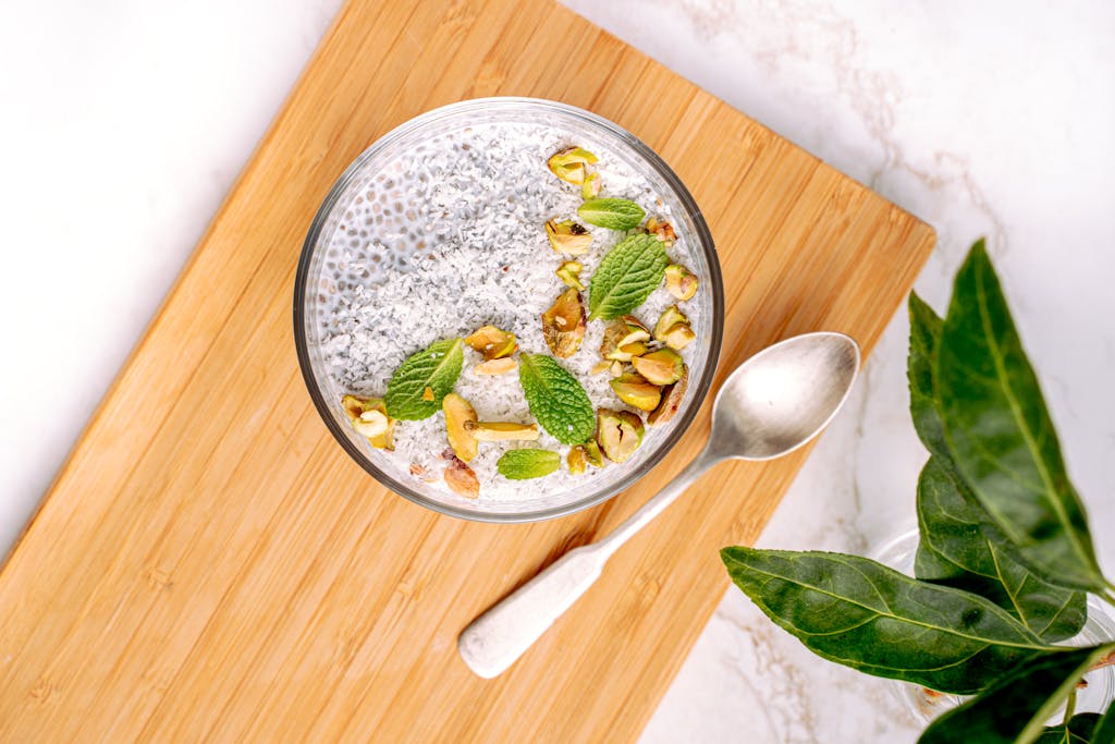 Top view of a chia seed pudding bowl garnished with pistachios and mint leaves on a wooden board.