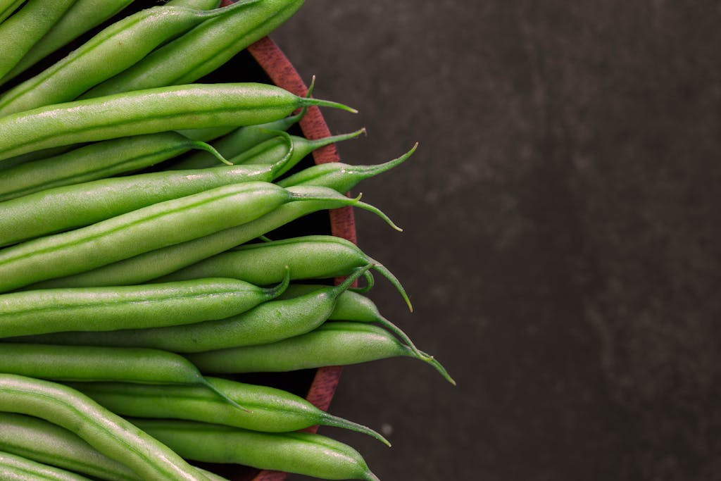 A close-up view of fresh green beans arranged in a rustic wooden bowl.