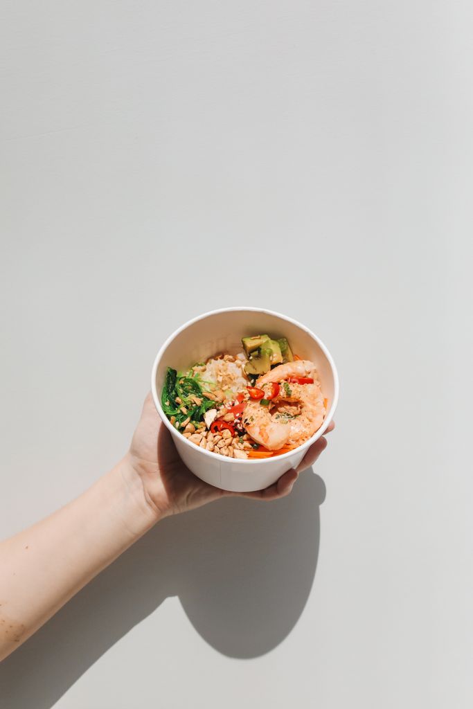 A delicious and colorful poke bowl with shrimp and vegetables, held in a hand against a simple background.