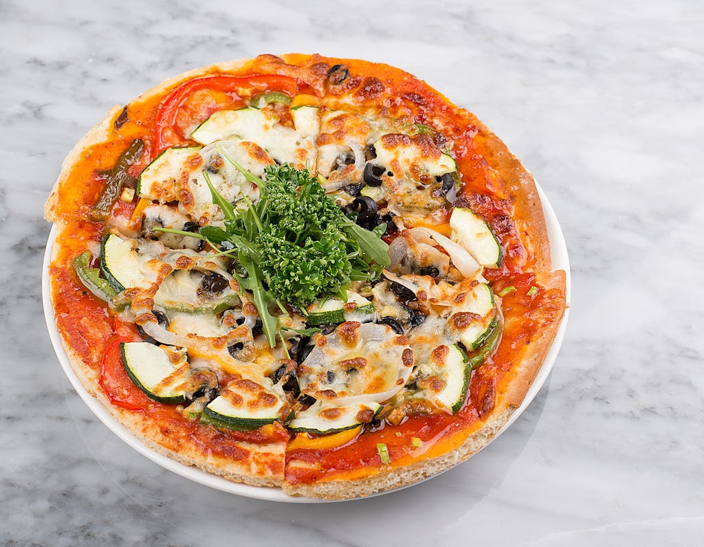A mouthwatering vegetarian pizza with cheese, olives, and fresh greens on a marble background.