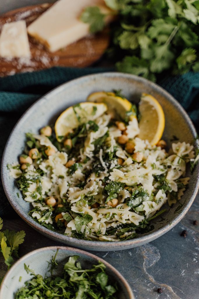 A vibrant bowl of pasta salad with fresh herbs, chickpeas, and lemon slices, perfect for a refreshing meal.