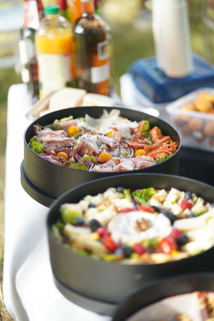 Close-up of a variety of fresh salads in bowls at an outdoor picnic with drinks in the background.