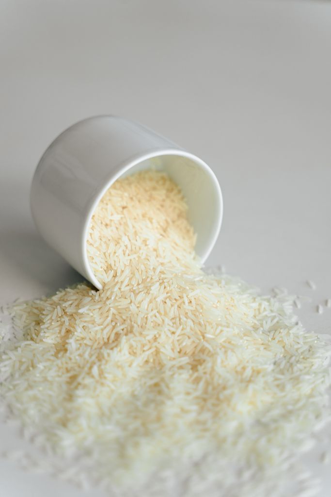 Close-up of uncooked rice spilling from a white cup, minimalist still life.