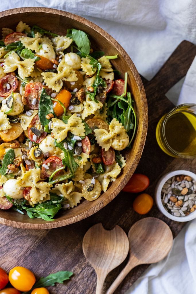 Delicious bowtie pasta salad with vibrant vegetables, arugula, and mozzarella in a wooden bowl.