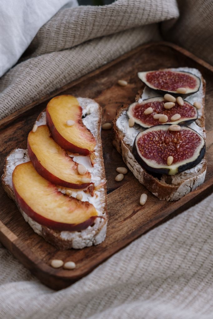 Delicious rustic sandwiches topped with fresh figs, peaches, and pine nuts on a wooden tray.