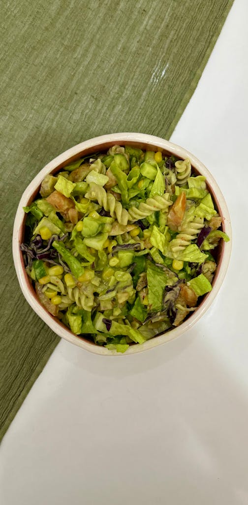 Healthy vegetable pasta salad with greens in a bowl on a textured surface.