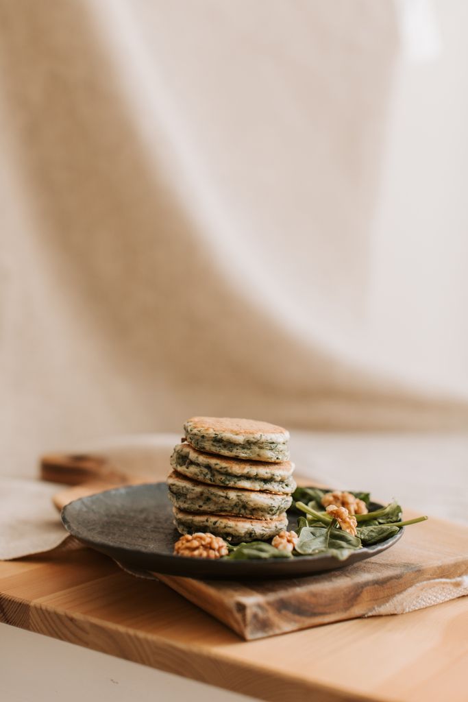 Savory pancakes stacked on a rustic plate with spinach and walnuts, perfect breakfast setting.