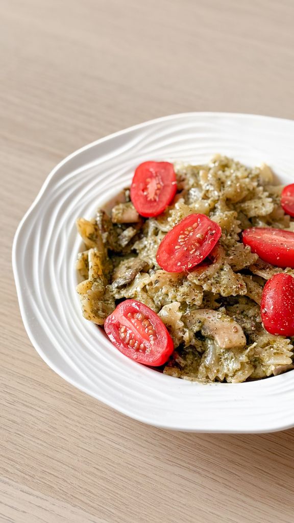 Tasty pesto pasta topped with cherry tomatoes on a white plate in a bright setting.