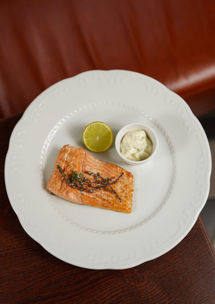 Top view of a grilled salmon fillet with lime and sauce on a white plate.
