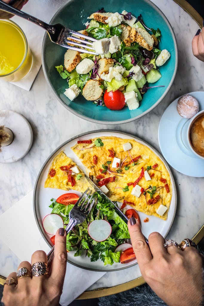 Vibrant brunch featuring an omelette and fresh salad bowls on a marble table.