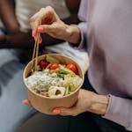 Person enjoying a nutritious salad bowl with fresh ingredients using chopsticks indoors.